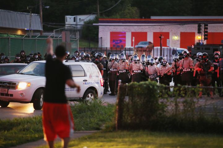 A man approaches a wall of police holding off protestors.