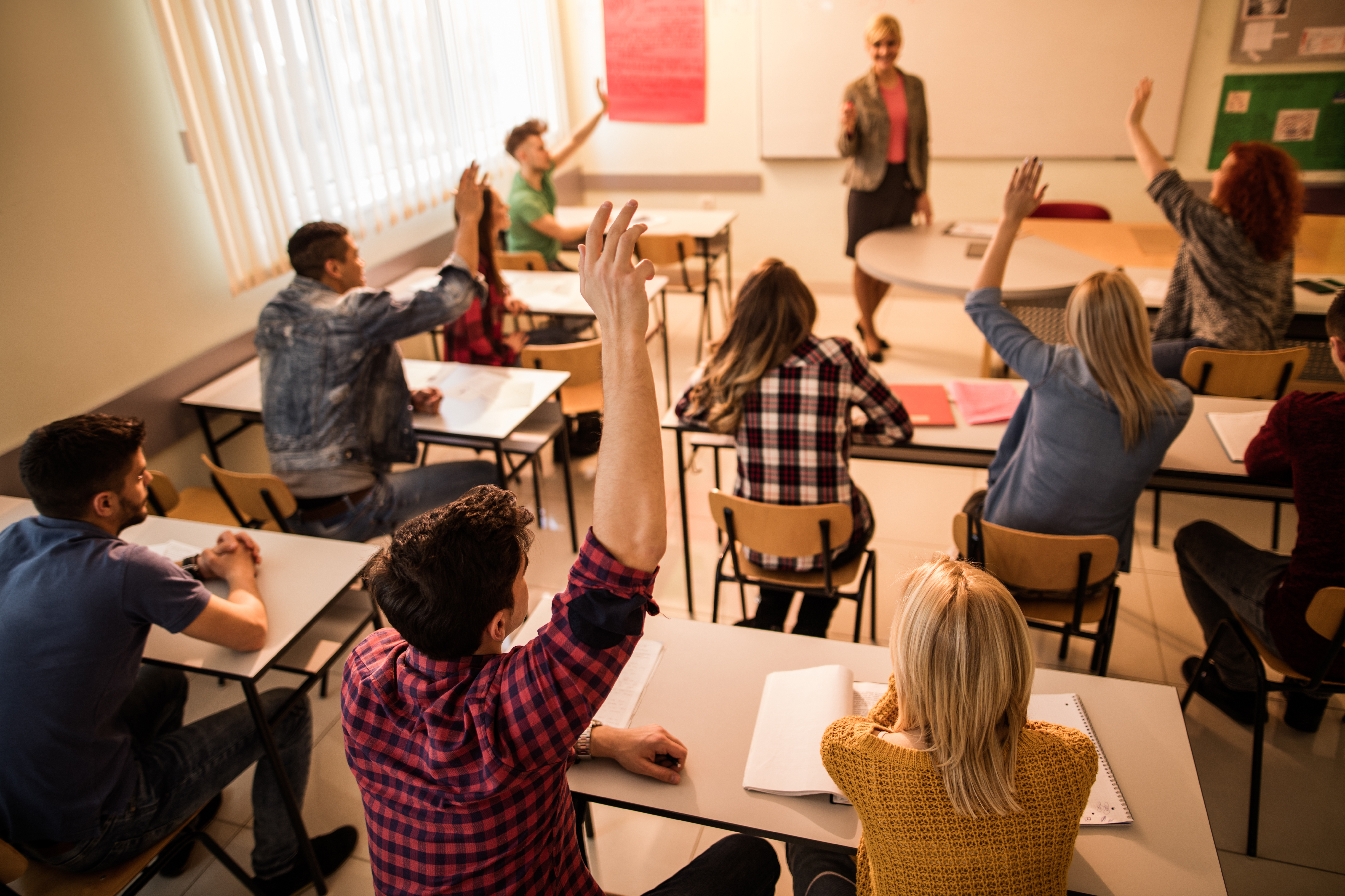 Students in the classroom raising hands to answer teacher's question.