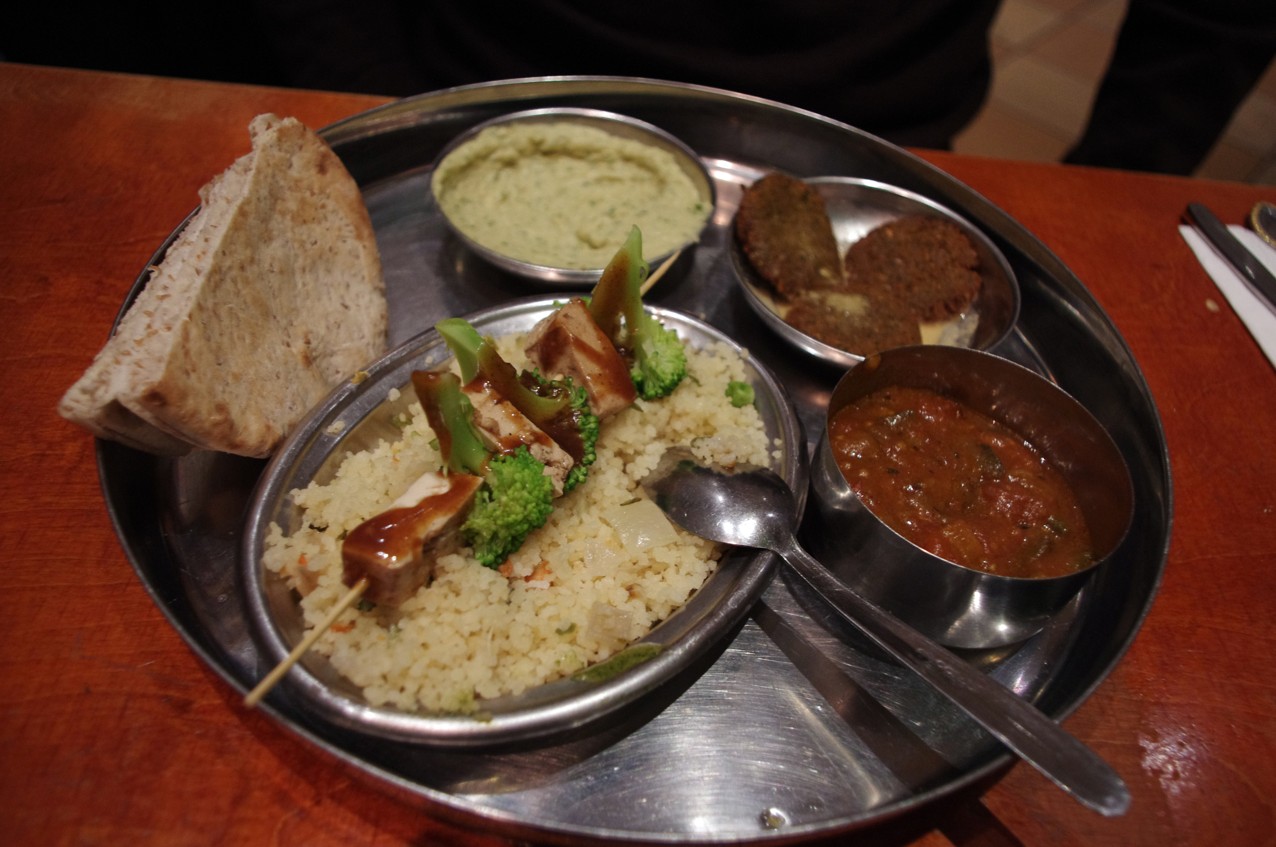 Vegetarian mezze platter with tofu and broccoli skewer with peanut sauce, couscous, pita bread, fava bean dip, falafel, and eggplant curry