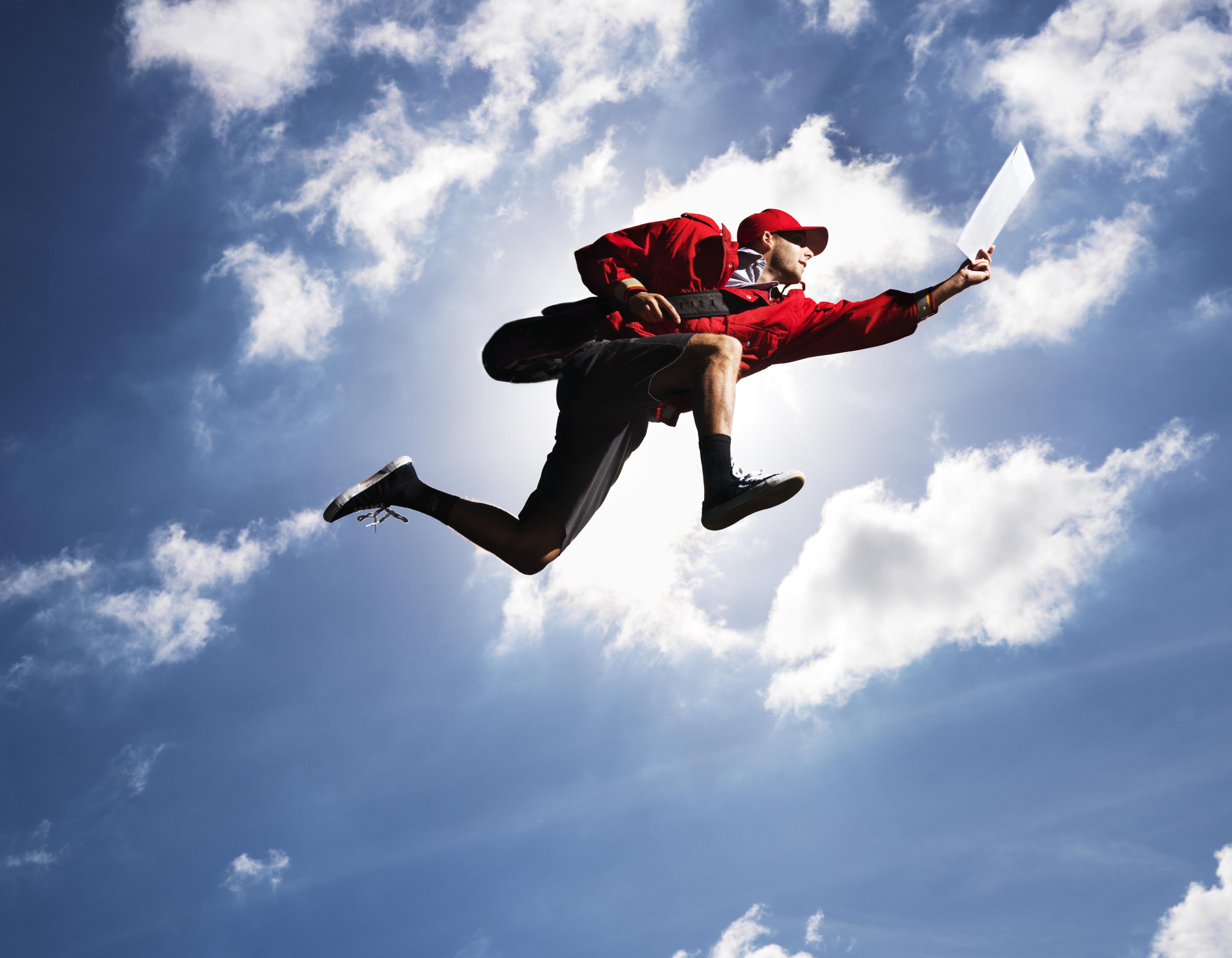 Man flying in air with letter in hand, against sky, low angle view