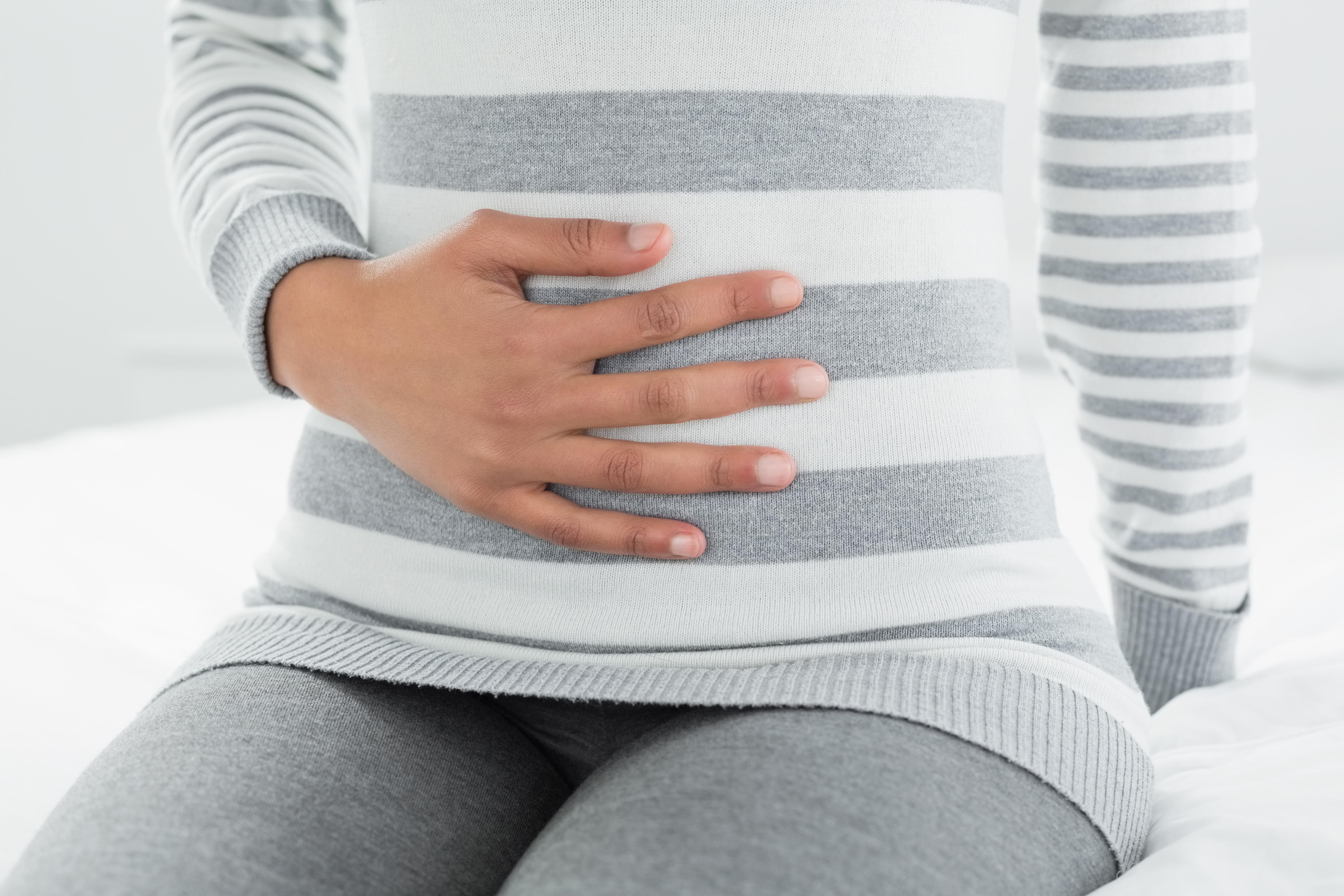 Close-up mid section of a casual young woman with stomach pain sitting in bed at home