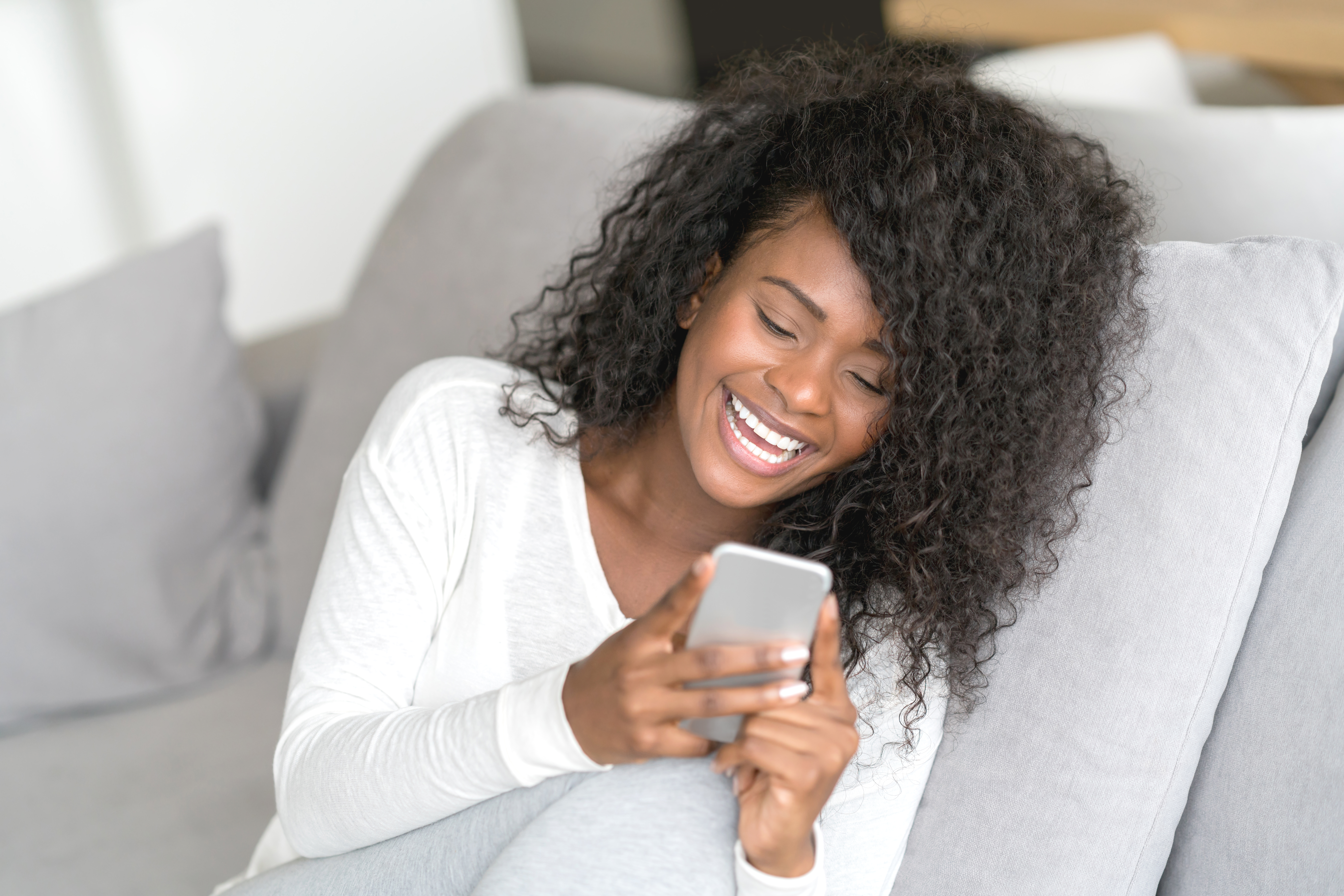 Beautiful female black woman chatting on her smartphone laughing while relaxing at home