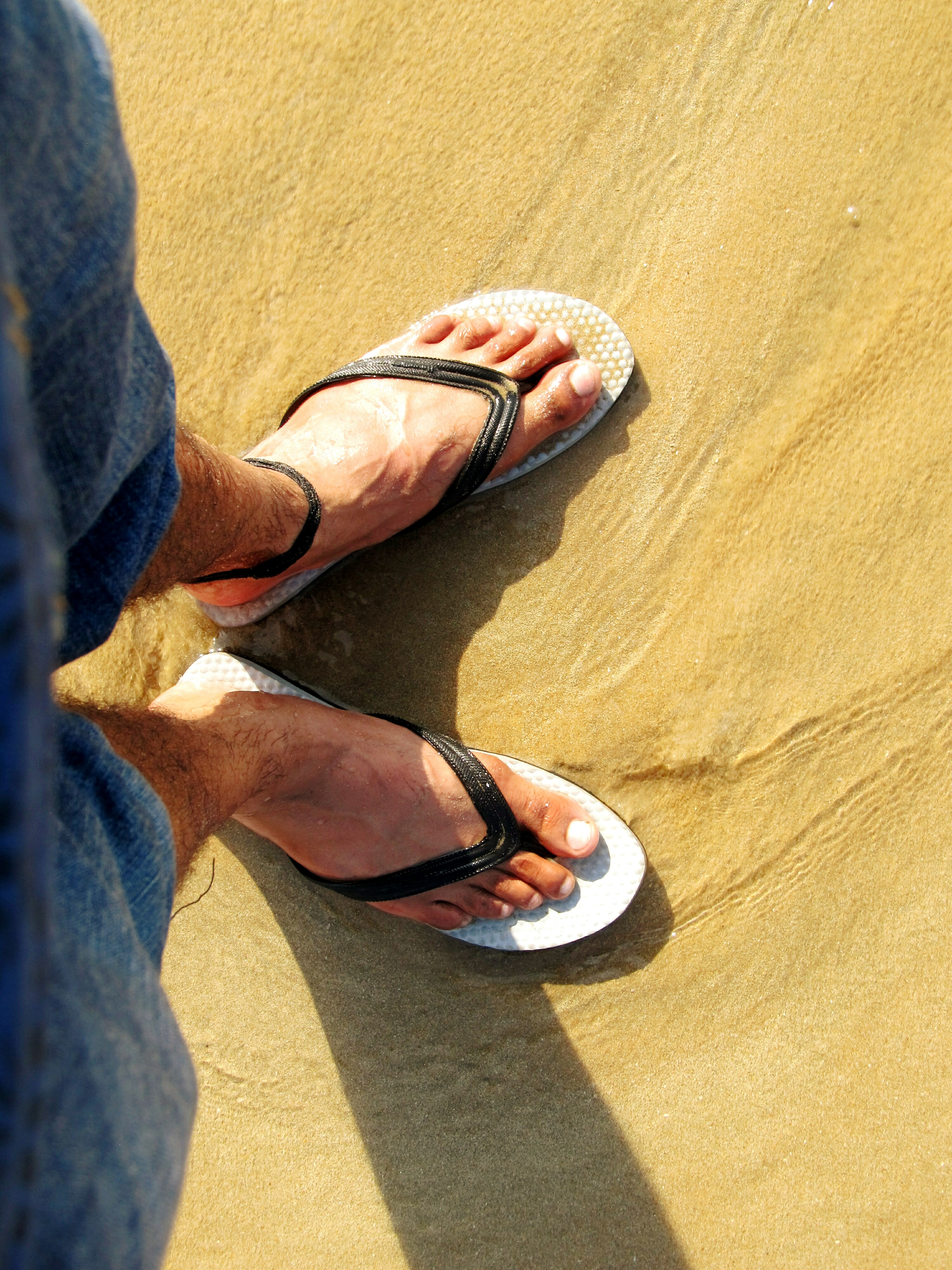Low Section Of Man Standing On Sand