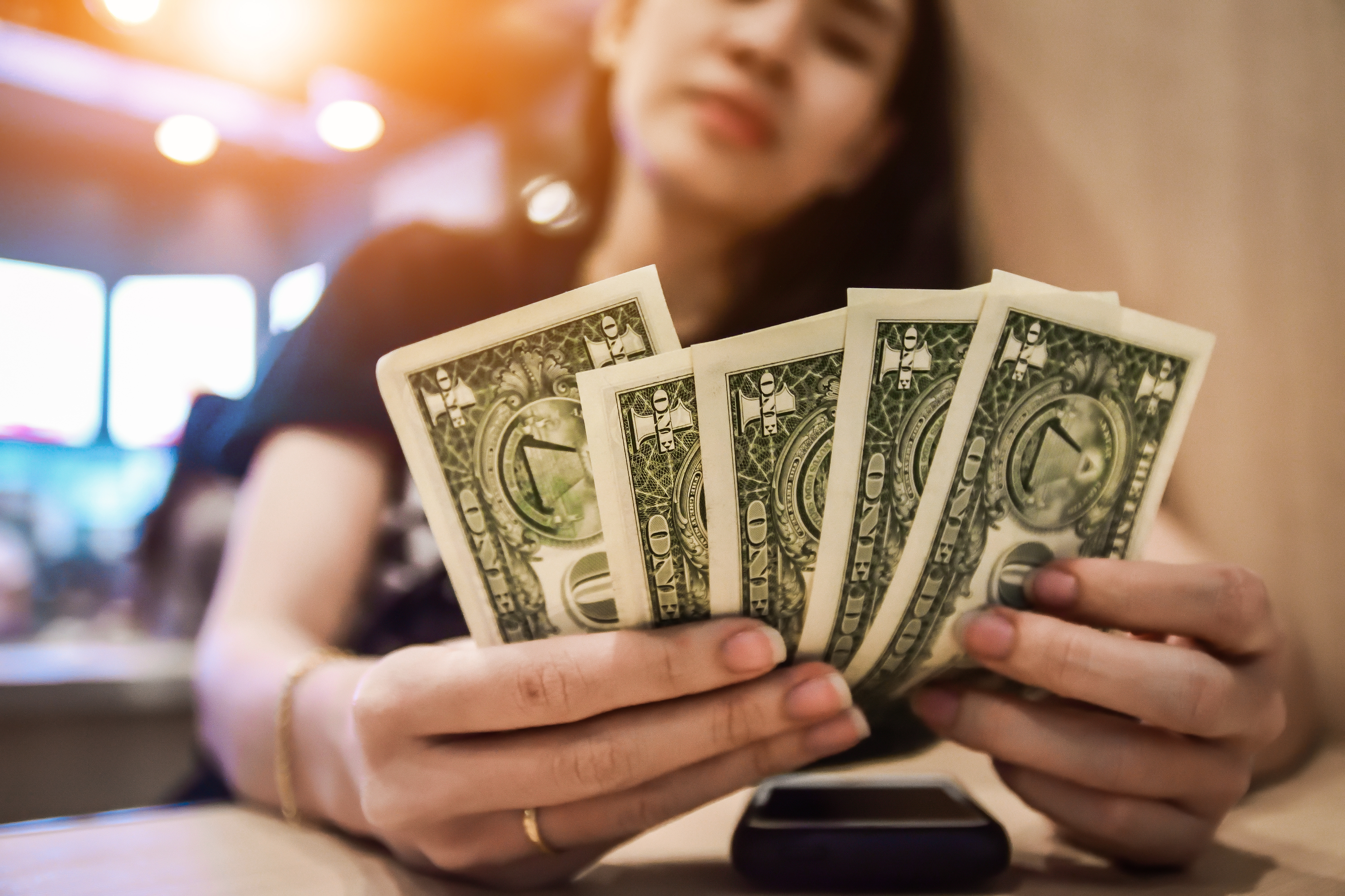 Close-Up Of Young Woman Holding Paper Currencies On Table