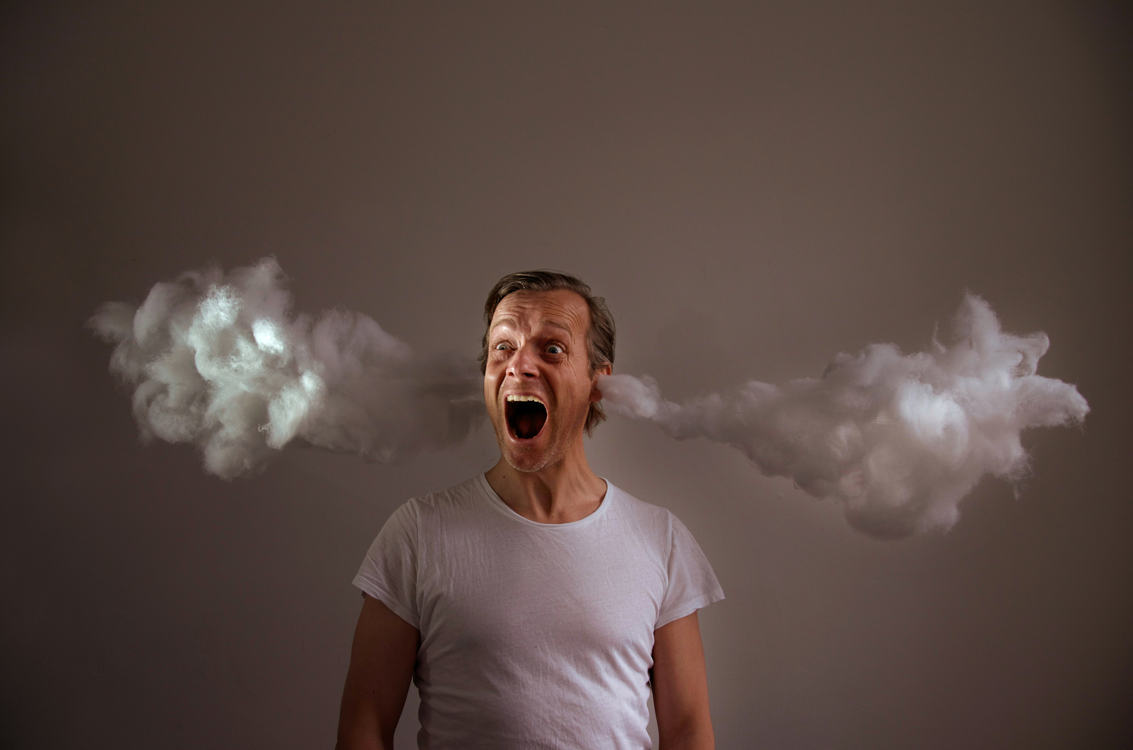 Screaming Man With Cotton Emitting From Ears Against Gray Background