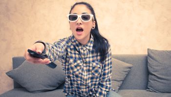 Young Woman Holding Remote Control While Sitting On Sofa At Home