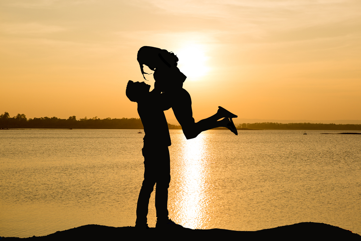 Silhouette Man Lifting Woman By Lake During Sunset