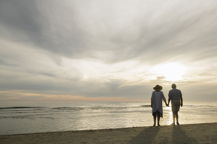 Back view of senior couple standing hand in hand on the beach watching sunset, Liepaja, Latvia