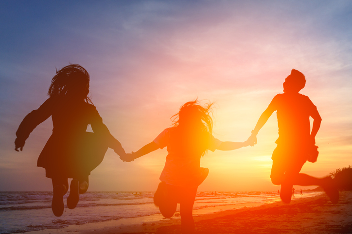 Silhouette Friends Holding Hands While Jumping At Beach Against Orange Sky
