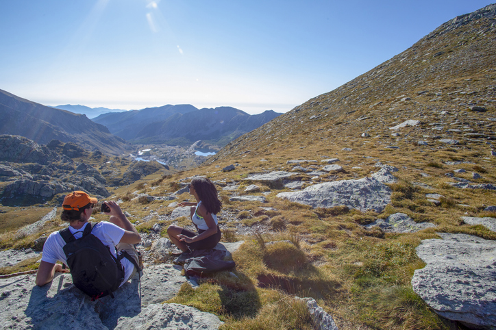 Hiking friends relax at trail summit, in grassy meadow