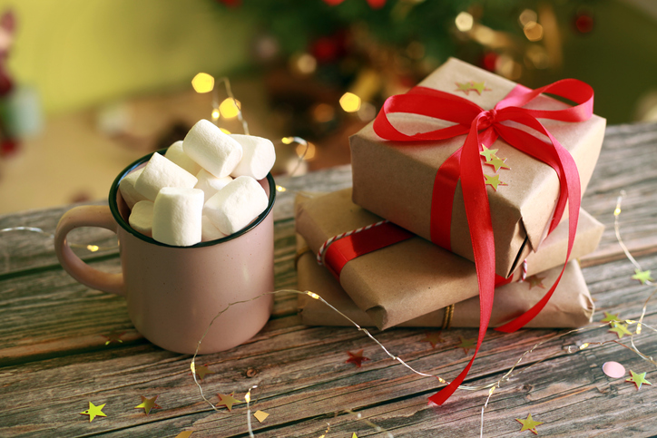 Gift boxes and pink cup with hot drink and marshmallow on table under Christmas tree