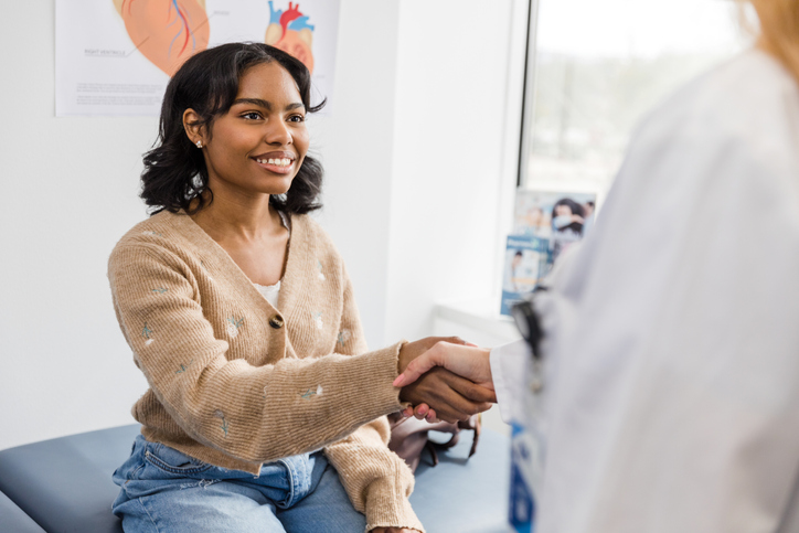 Smiling young woman reaches out to shake unrecognizable doctor's hand