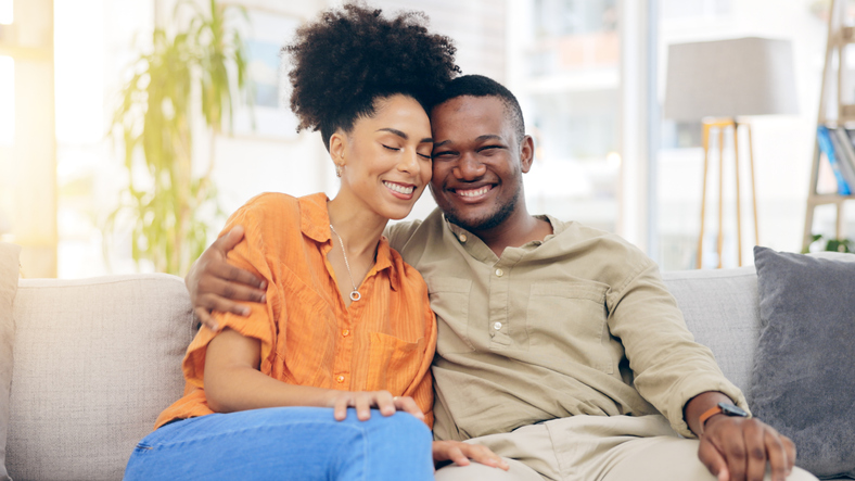 Happiness, love and couple hug, relax and bonding together on lounge couch with partner care, support and trust. Smile, home wellness and black man, woman or marriage people hugging in South Africa