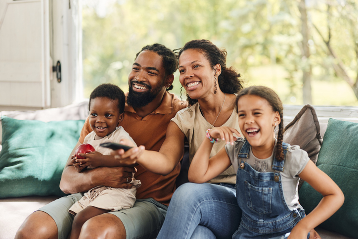 Happy black family watching TV on sofa at home.