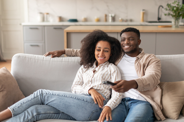 Black millennial couple watching TV in their cozy living room