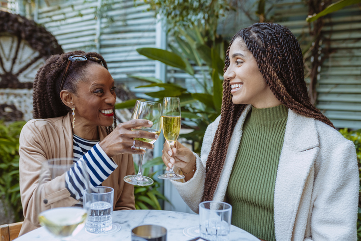 Two cheerful black women toasting with white wine in a restaurant