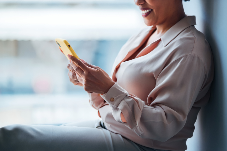 Smiling Woman Using a Yellow Smartphone While Sitting Indoors