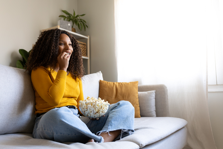 Young woman watching tv and eating popcorn on sofa at home