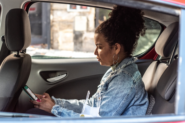 Mid adult woman using mobile phone in the passenger seat inside the car
