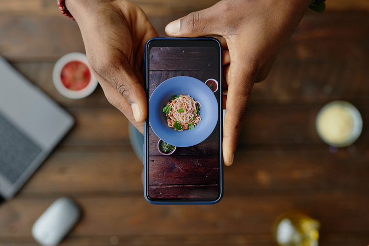 Person Photographing Pasta Dish with Smartphone over Wooden Table