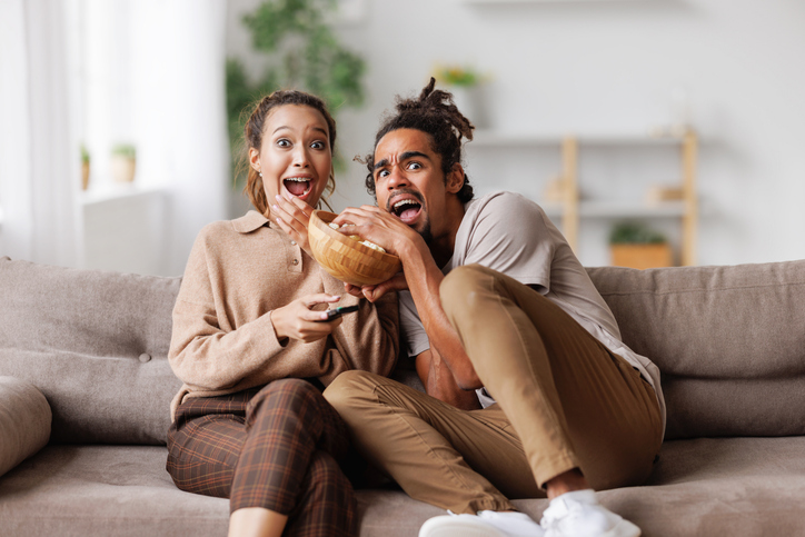 Young scared african american family couple screaming while watching horror movie at home